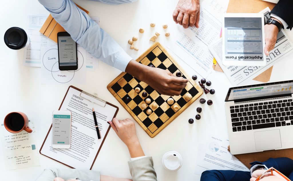 Algumas pessoas jogando xarex sobre uma mesa com material de escritório, representando estratégias para conquistar oportunidades de negócios