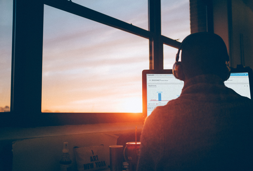 Um homem com a Advbox aberta na tela do computador em frente a uma janela com o sol se pondo. Os gráficos na tela demonstram os custos fixos do escritório