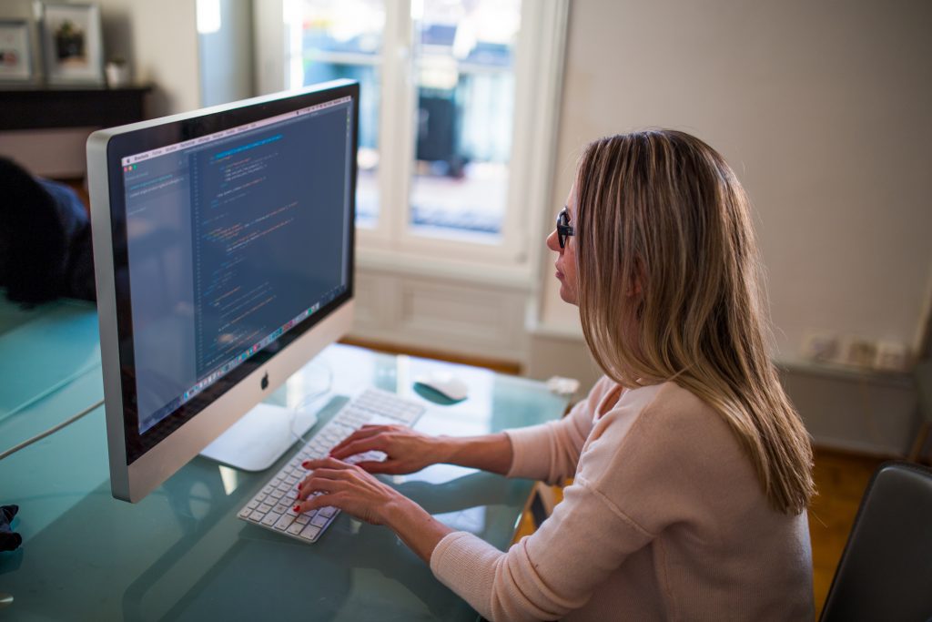 Mulher mexendo no computador com a tela exibindo códigos de programação, representando a capacidade de robôs de andamentos processuais automáticos