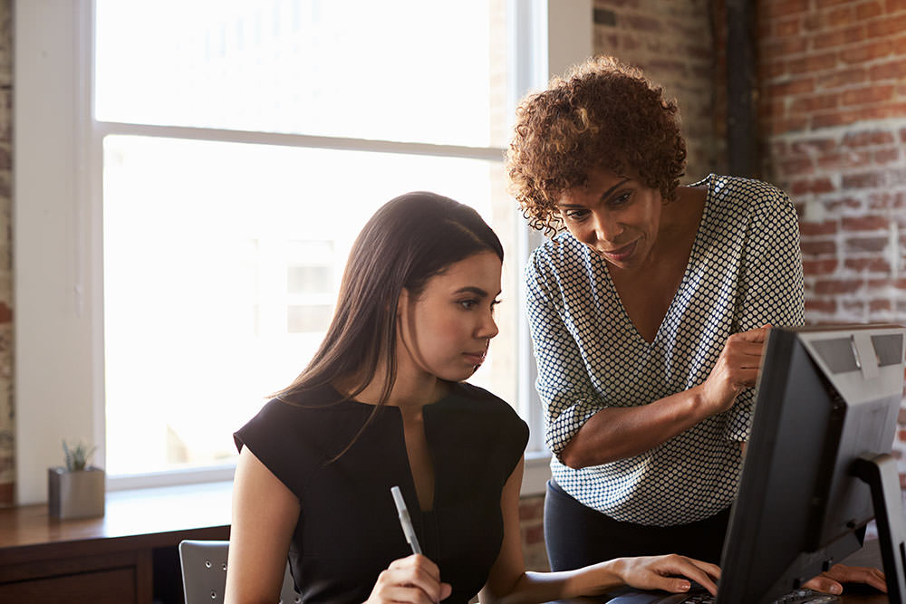 Duas mulheres olhando para uma tela de computador em um escritório e aprendendo a usar um Software jurídico