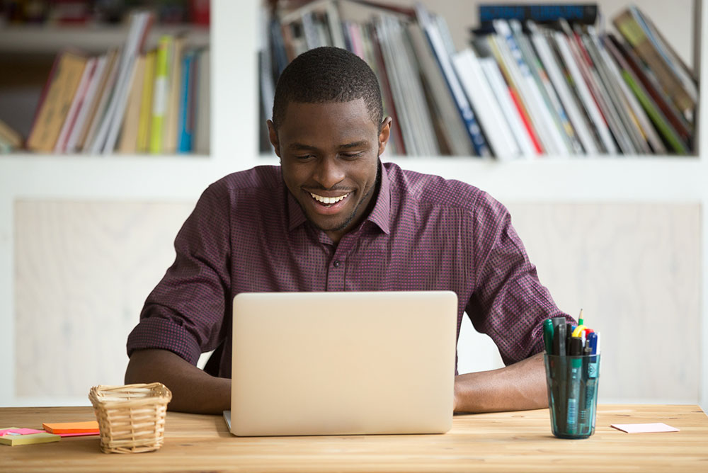 Um homem sorrindo em frente a um notebook sobre uma mesa, demonstrando as facilidades de um atendimento jurídico otimizado