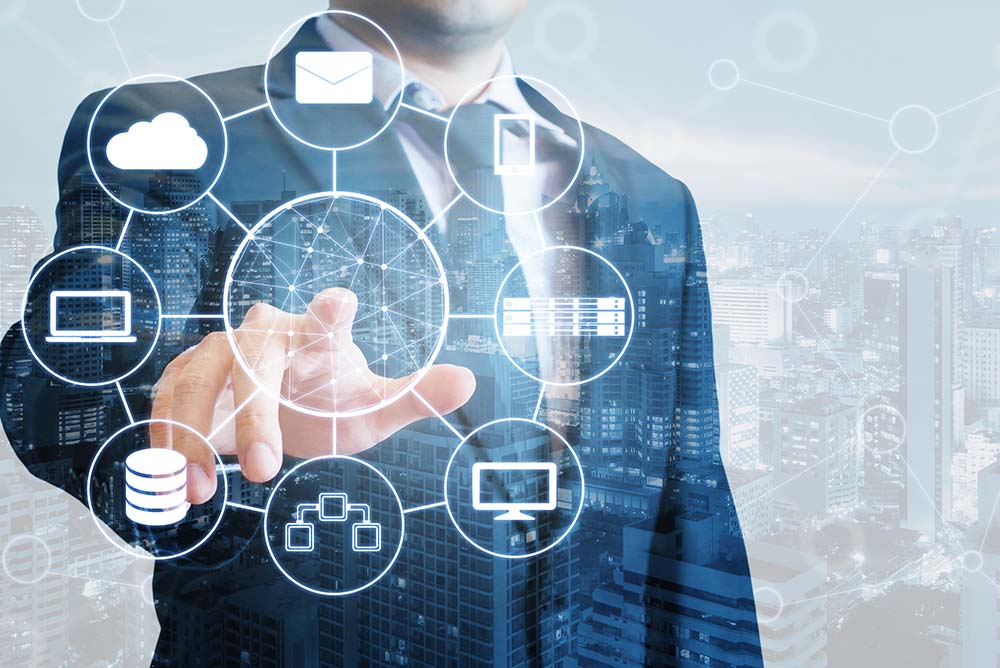 Um homem de terno tocando em uma superfício de vidro onde surgem diversos elementos relacionados à tecnologia, como engrenagens, computadores, celulares e tablets. Representa as possibilidades de ferramentas para potencializar seu escritório